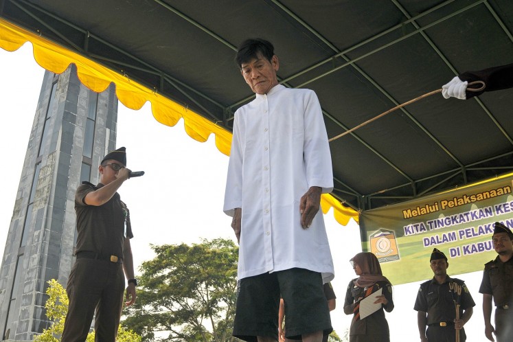 Going sharia: A man stands in front of officers before being caned for gambling outside Al Munawaroh Mosque in Jantho, Aceh Besar regency, Aceh, on Friday. Despite being Buddhist, two people who were recently caught participating in cockfighting opted for caning as punishment instead of facing criminal charges.