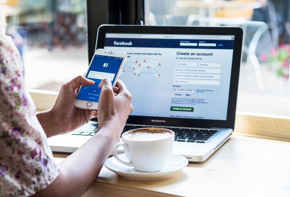 A man opens a Facebook page on his laptop, while monitoring his smartphone. (Shutterstock/File)