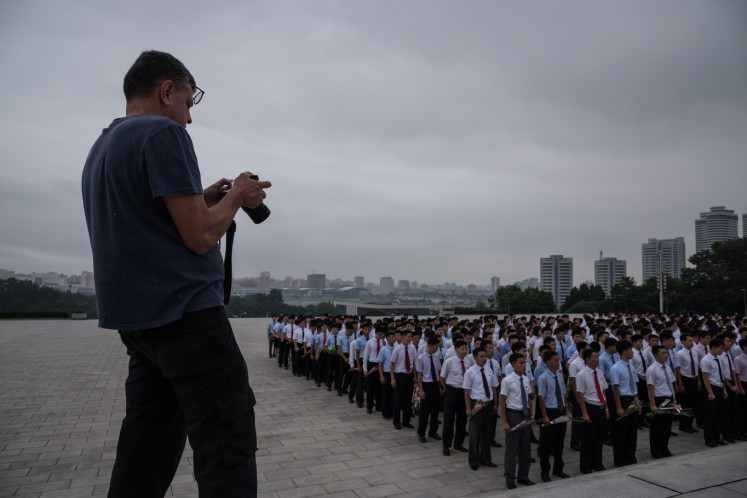 A tourist takes photos before a group of people gathered to pay their respects before statues of late North Korean leaders Kim Il-Sung and Kim Jong-Il on Mansu hill in Pyongyang on July 23, 2017.