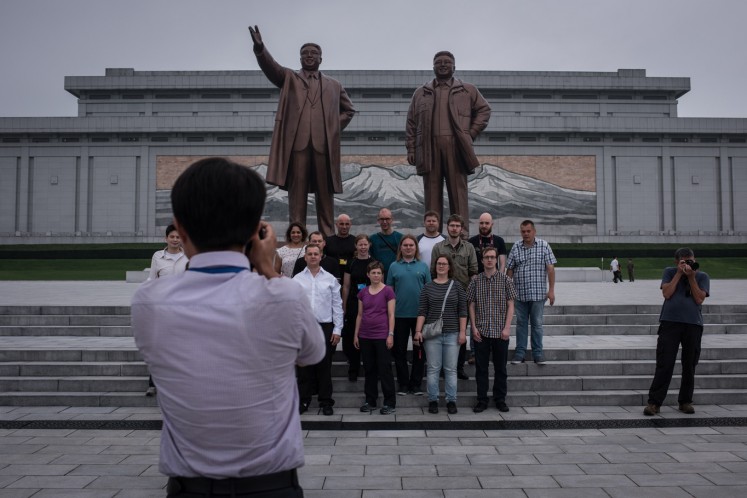 Tourists pose for a group photo before statues of late North Korean leaders Kim Il-Sung (L) and Kim Jong-Il (R), on Mansu hill in Pyongyang on July 23, 2017.