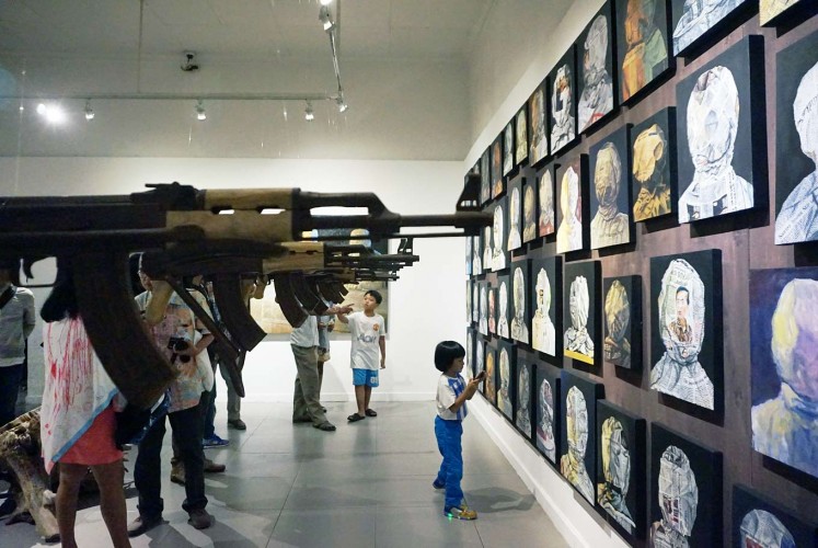 The trigger: A giant AK4 rifle points at images of wrapped faces on the wall.