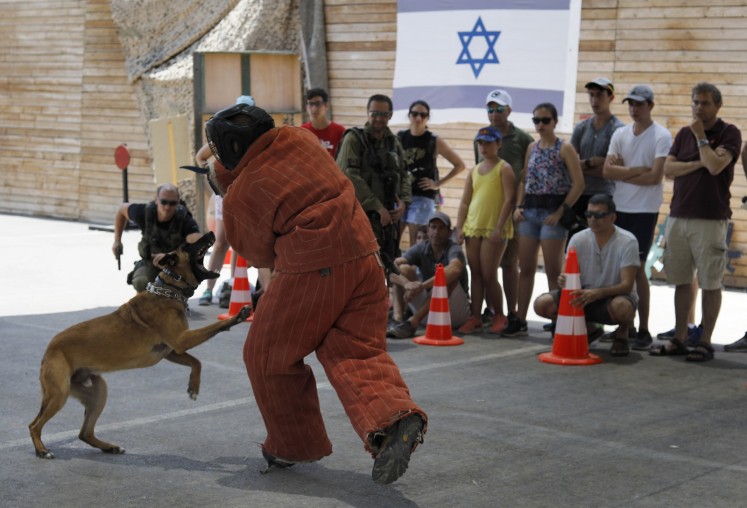 Foreign tourists watch an Israeli instructor demonstrating how to use a dog to neutralize an attacker during a simulation.