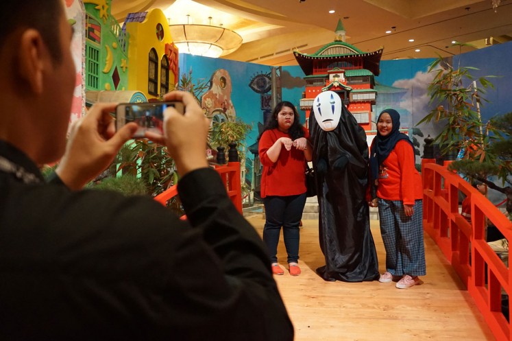 Two female visitors take pictures with Kaonashi with the help of one of the exhibition's attendants at The World of Ghibli Jakarta exhibition.