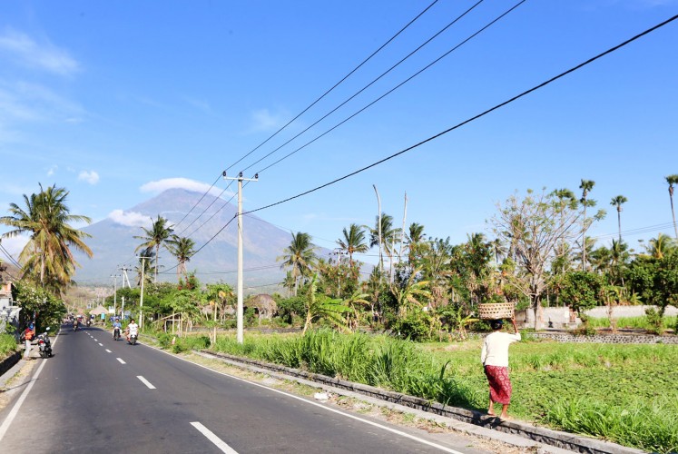 Deceptively calm: People go about their daily activities in the shadow of the rumbling Mount Agung in Bali.