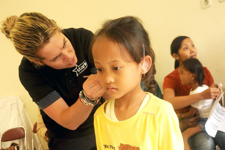 Incoming sounds: A girl stands still as a volunteer attaches the hearing aid.