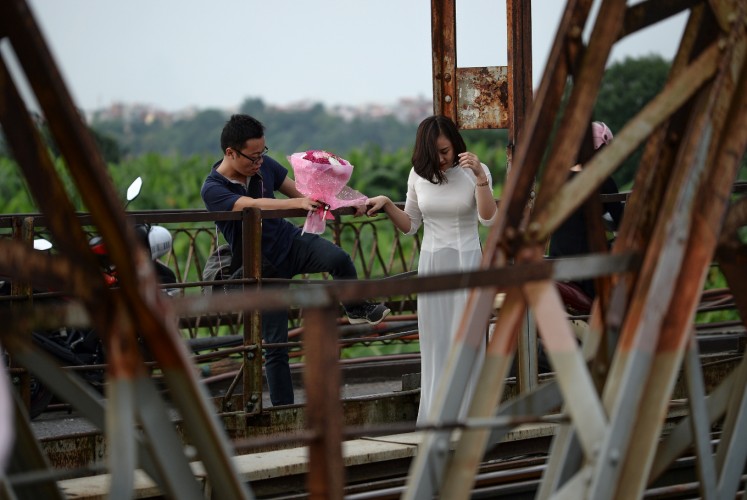 In this photograph taken on October 20, 2017, a man holding a bunch of flowers, climbs over a railing to follow a woman at a century old bridge built by the French and a popular destination for lovers to go and take photographs. Shuffling through Vietnam's 