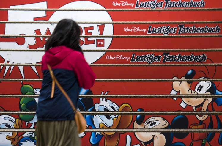A young woman stands in front of stairs which have been covered with an advert to mark the 50th anniversary of the German version of the Donald Duck pocket books at a metro station in Berlin.