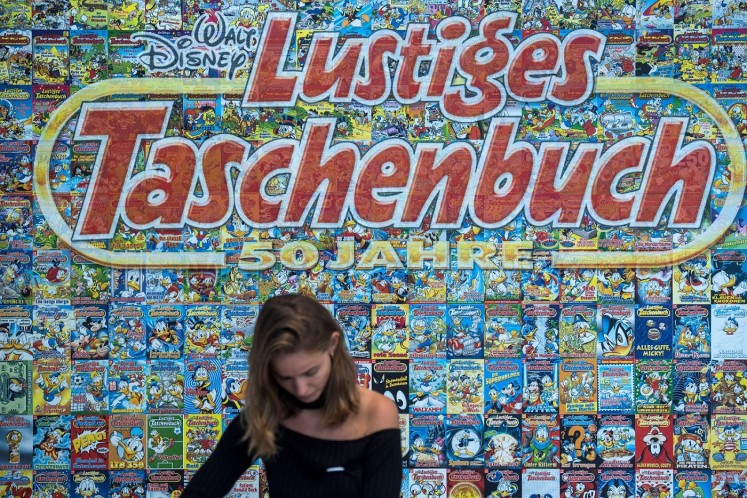 An employee stands behind a cashier desk in front of a backdrop made up of hundreds of covers of Donald Duck pocket books.