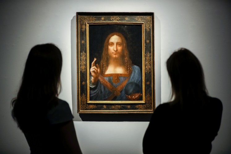 Christie's employees pose in front of a painting entitled Salvator Mundi by Italian polymath Leonardo da Vinci at a photocall at Christie's auction house in central London on October 22, 2017 ahead of its sale at Christie's New York on November 15, 2017. 