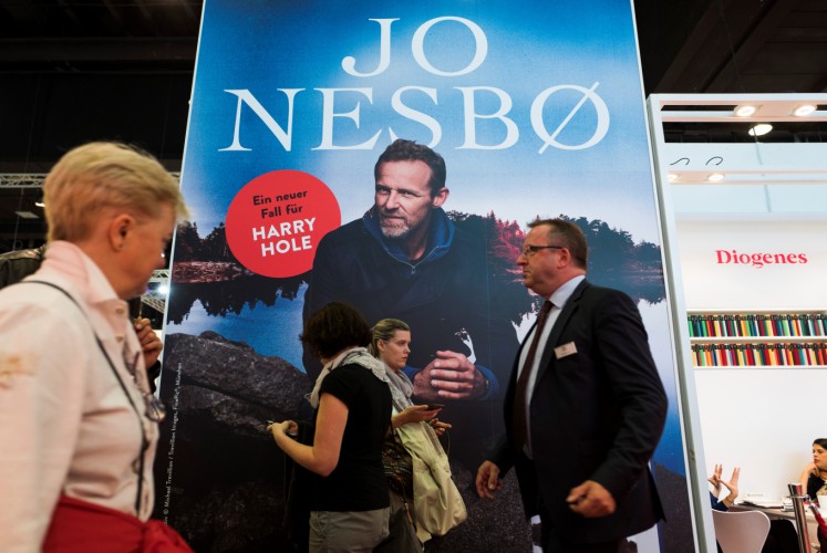 Visitors walk past a poster promoting best-selling Norwegian crime writer Jo Nesbo at the Frankfurt Book Fair on October 13, 2017 in Frankfurt am Main, western Germany. France is this year's guest of honour at the world's largest book fair, where more than 7,000 exhibitors from more than 100 countries are expected from October 11 to 15.