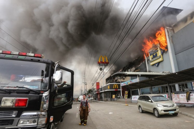This photo taken on December 23, 2017 shows a firefighter standing in front of a burning shopping mall in Davao City on the southern Philippine island of Mindanao. Thirty-seven people were believed killed in a fire that engulfed a shopping mall in the southern Philippine city of Davao, local authorities said on Dec. 24.