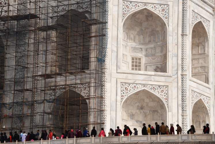 In this photograph taken on January 3, 2018, visitors walk past scaffolding erected for conservation work at the Taj Mahal in the Indian city of Agra. Restoration work at India's most popular tourist attraction has been dragging on for years, blighting views for tourists, but authorities have not even begun work on the unmissable centrepiece of the 17th-century icon -- its imposing dome.