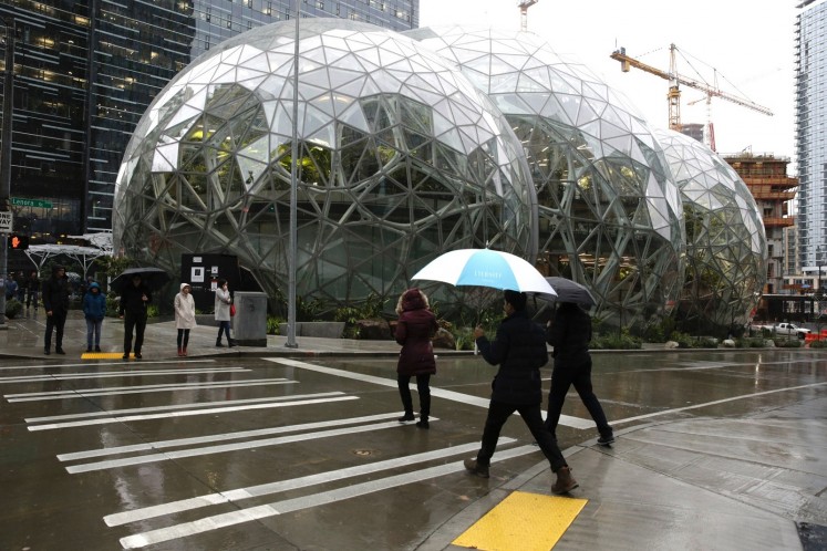 People walk past the Amazon Spheres, in Seattle, Washington on January 29, 2018, during the grand opening of the company's new office space.  Amazon opened its new Seattle office space which looks more like a rainforest. The company created the Spheres Complex to help spark employee creativity. 