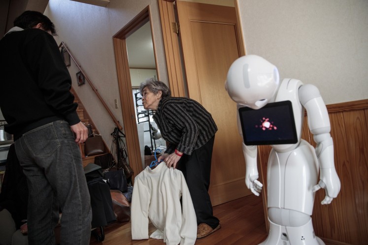 In this picture taken on January 16, 2018, Kimiko Nishimoto consults with her son Kazutami to select a costume for a photoshoot as her humanoid robot called Pepper (R) is seen at her house in the western Japanese city of Kumamoto. 