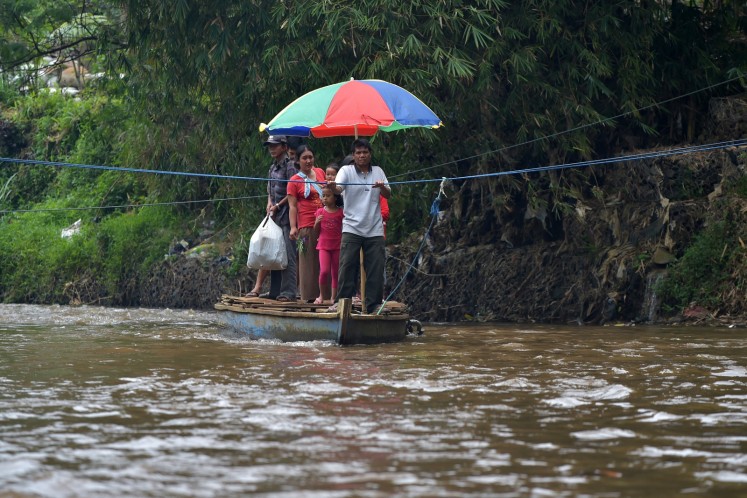 This picture taken on February 5, 2018 shows people crossing the Citarum river in a boat in Majalaya, West Java. Now faced with a health emergency after decades of failed clean-up efforts, Jakarta is stepping in with a seemingly impossible goal: make the Citarum river's water drinkable by 2025.