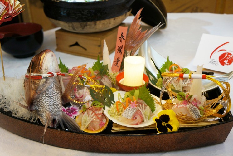A platter features an elaborately garnished 'sugata-zukuri' (red sea bream sashimi), using radishes, bamboo leaves and carrots, as well as the fish's head and body.