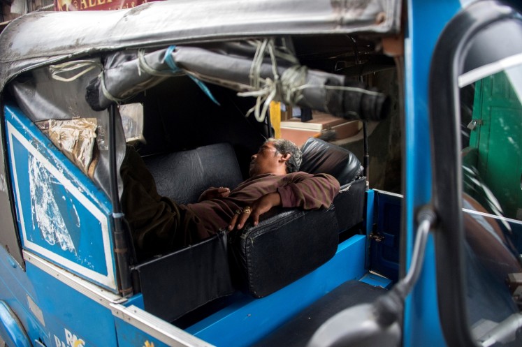 This photograph taken on February 13, 2018 shows a three-wheeled bajaj taxi driver taking a nap while waiting for passengers in Jakarta.