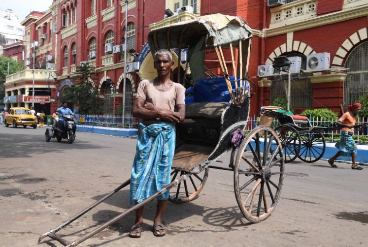 Mohammad Ashgar, 65, an Indian rickshaw puller, poses for a photograph next to his rickshaw in Kolkata on April 21, 2018. 
