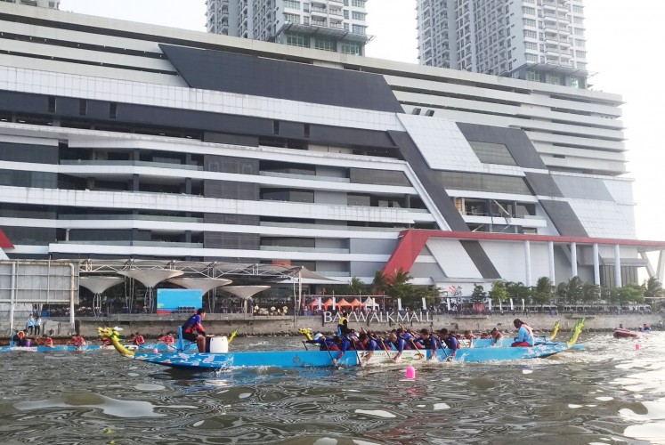 A team paddling a turquoise dragon boat competes in the 2018 Jakarta Dragon Boat Festival past the cruise ship-like facade of Baywalk Mall in Pluit, North Jakarta.