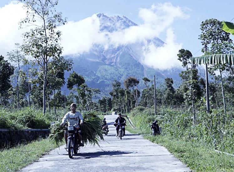 Daily routine: Residents carrying grass for their livestock pass a road in Tlogolele village, Selo district, Boyolali regency, Central Java, as thick smoke emanates from the crater of Mount Merapi. 
