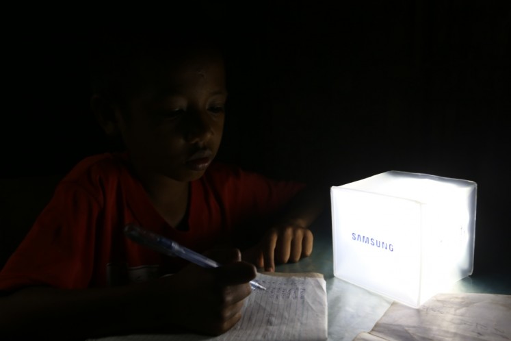 A boy studies beside a solar-powered lantern. 