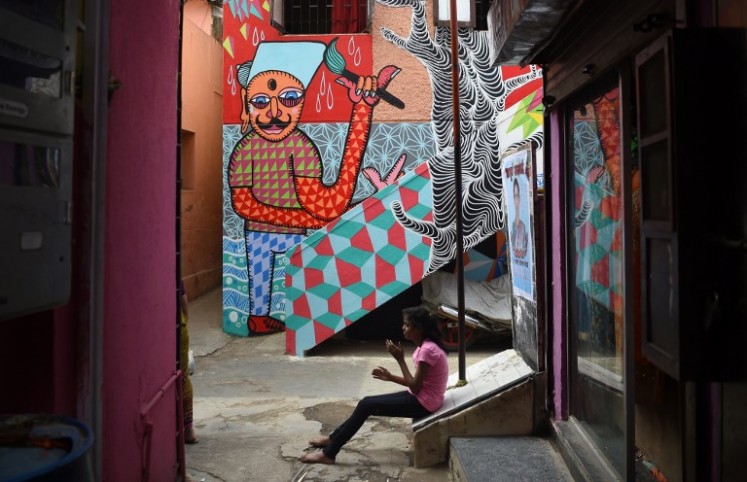 In this picture taken on June 1, 2018, an Indian girl sits near a mural in Mumbai.