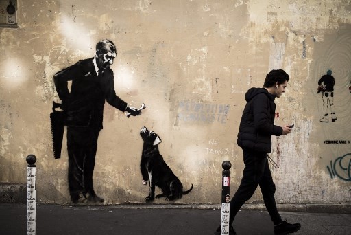 A man walks past a recent artwork by street artist Banksy in Paris on June 24, 2018. Anonymous street artist Banksy's artwork of a man holding a handsaw behind his back and offering a bone to a dog which leg has been cut off, has been found near the Sorbonne University, in the center of Paris over the weekend. 