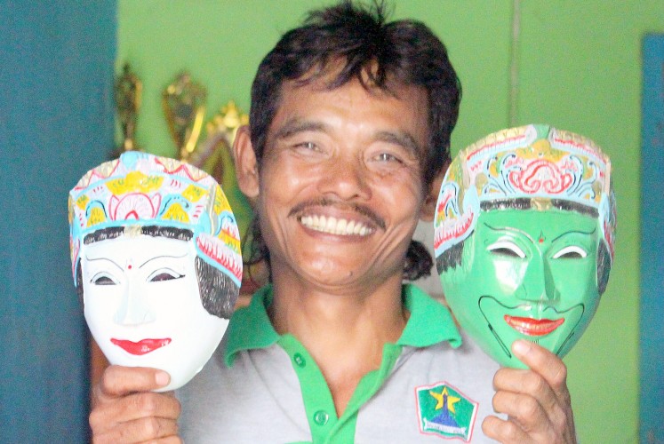 A display of craftsmanship: Mask artisan Prasetiyo Hadi poses with two masks at his shop in Kampung Topeng.