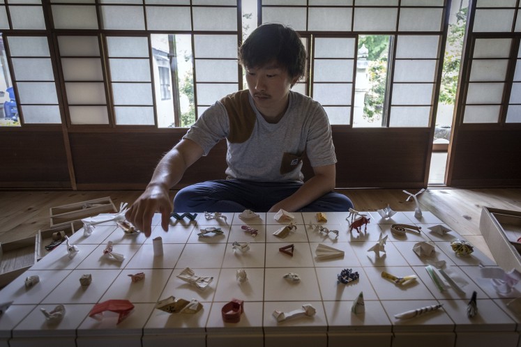 In this picture taken on May 23, 2018, Yuki Tatsumi sits next to his collection of origami made from chopstick sleeves in Kameoka, Kyoto prefecture. 