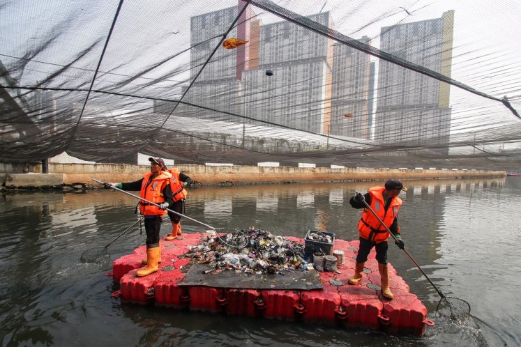 City workers clean the Sentiong River under a giant nylon net in Central Jakarta on July 21. The city administration covered the river in an attempt to ward off the smell ahead of the 18th Asian Games in August.