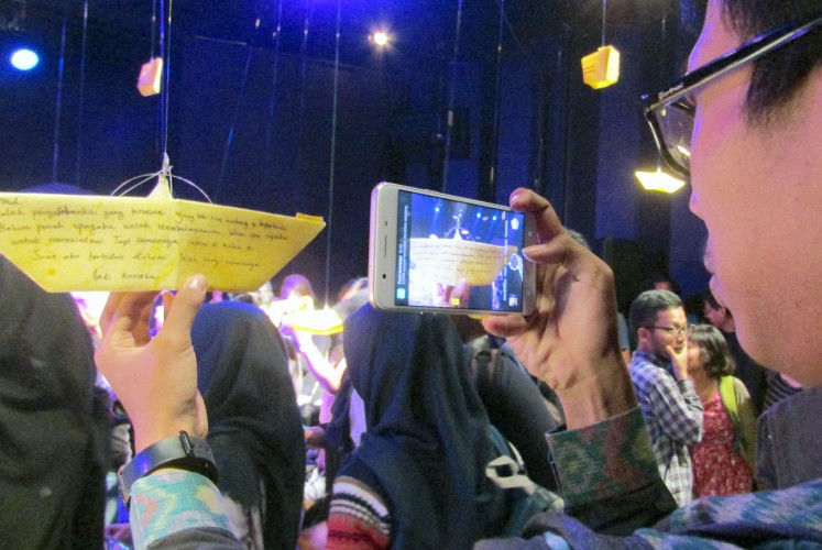 Remembrance: An audience member photographs a paper boat bearing a message written to a deceased loved one. 