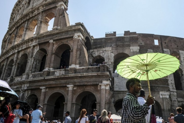 A man holds an umbrella to protect himself from the sun during a ho Summer day in front of the Ancient Colosseum in central Rome on August 2, 2018, as Italy is experiencing a summer heatwave with temperatures approaching 40 degrees Celsius.