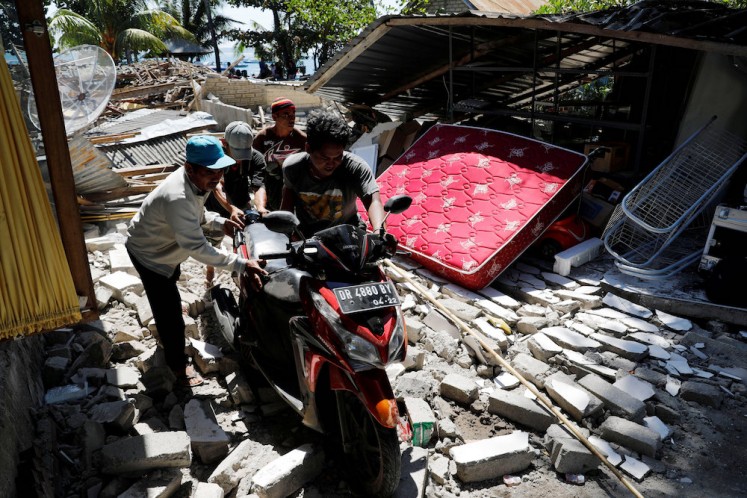 Villagers push a motorcycle along ruins after an earthquake hit Lombok island in Pamenang, Indonesia August 6, 2018. REUTERS/Beawiharta