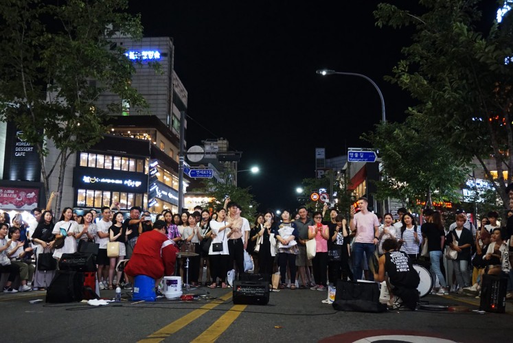 Visitors watch a music performance by street artists in Yonsei-ro.