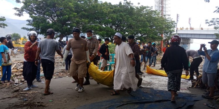 Survivors and police personnel retrieve bodies near Ponulele Bridge above Talise Bay in Palu city on Sept. 29, 2018.
