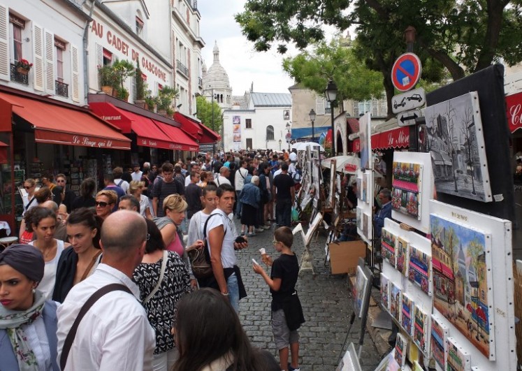 This file photo shows tourists look at the work of painters in Place du Tertre in the Montmartre district of Paris on August 16, 2015. 