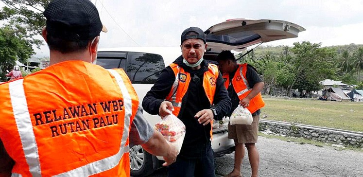 Helping hand: Inmates from the Palu detention center in Central Sulawesi, clad in neon orange vests, help distribute food packages to a number of temporary shelters across the city where survivors of the earthquake and tsunami are living.