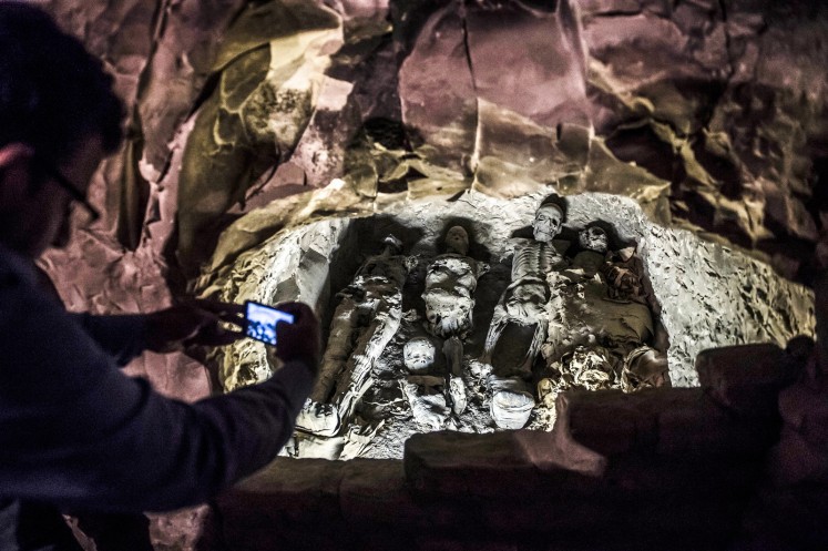 This picture taken on November 24, 2018 shows a man using a cell phone to take a picture of a group of mummies stacked together at the site of Tomb TT28, which was discovered by an Egyptian archaelogical mission at Al-Assasif necropolis on the west bank of the Nile north of the southern Egyptian city of Luxor. Located between the royal tombs at the Valley of the Queens and the Valley of the Kings, the Al-Assasif necropolis is the burial site of nobles and senior officials close to the pharaohs.