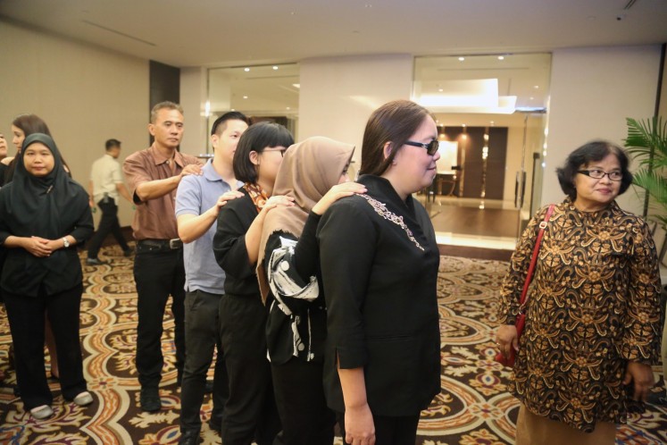 A visually impaired server from Yayasan Mitra Netra guides four journalists into Fairmont Jakarta's ballroom during the Dining in the Dark media event on Tuesday. 