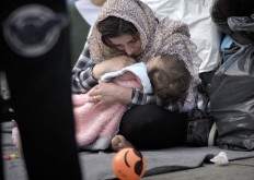 A migrant woman cries while holding a baby, in Athens, Monday, Feb. 29, 2016, at the Victoria Square, where most newly-landed migrants head after reaching the Greek capital from the Aegean Sea islands. Border restrictions further north in the Balkans have left thousands of refugees and other migrants stranded in a country that is still wracked by its own financial crisis and unable to seal its lengthy sea border with Turkey.
