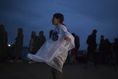 A girl wearing a  plastic rain poncho walks as refugees and migrants wait to receive food distributed by non-governmental organization at the Greek-Macedonian border, in the northern Greek village of Idomeni, on Monday, Feb. 29, 2016.  Some 7,000 migrants, including many from Syria and Iraq, are crammed into a tiny camp at the Greek border village of Idomeni, and hundreds more are arriving daily. 