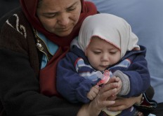 A Migrant woman holds a baby, in Athens, Monday, Feb. 29, 2016, at the Victoria Square, where most newly-landed migrants head after reaching the greek capital from the Aegean Sea islands. Border restrictions further north in the Balkans have left thousands of refugees and other migrants stranded in a country that is still wracked by its own financial crisis and unable to seal its lengthy sea border with Turkey.