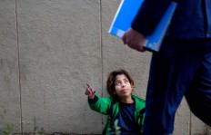 In this Wednesday, March 16, 2016 photo, a Syrian refugee girl begs for money on a sidewalk outside a hospital in Beirut, Lebanon. It is one of the most visible signs of the refugee crisis that has put an immense strain on neighboring countries and destabilized Europe. On Lebanon shopping streets, roundabouts and traffic lights, child beggars are seen pressing their small faces against windows of cars, stretching their hands for money or selling chewing gum or flowers.