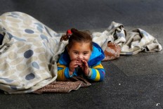 In this Wednesday, Feb. 10, 2016 photo, a Syrian refugee girl sits on the sidewalk with her mother as they beg for money, in Beirut, Lebanon. A study published last year by the International Labor Organization, UNICEF and the Save the Children charity organization found there are more than 1,500 children living or working on Lebanon's streets, nearly three-quarters of them Syrian and most making a living by begging. 