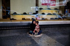 In this Tuesday, March 15, 2016 photo, a Syrian refugee woman holds her child as she begs for money on a sidewalk, in Beirut. Lebanon is home to more than 1 million registered Syrian refugees, or nearly a quarter of the country's 4.5 million people, the highest refugee population in the world per capita. It is one of the most visible signs of the refugee crisis that has put an immense strain on neighboring countries and destabilized Europe. On Lebanon shopping streets beggars are seen stretching their hands out for money. 