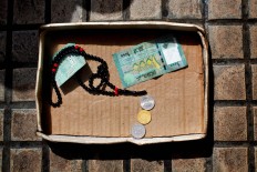 This Friday, March 25, 2016 photo, shows a cardboard box with money and praying beads belonging to a Syrian refugee woman who fled form her hometown Aleppo, on a sidewalk in Beirut, Lebanon. Begging is one of the most visible signs of the refugee crisis that has put an immense strain on neighboring countries and destabilized Europe. On Lebanon shopping streets, roundabouts and traffic lights, child beggars are seen pressing their small faces against windows of cars, stretching their hands for money or selling chewing gum or flowers. 