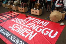 The women sit in a row behind a banner reading “Farmers shackled by cement” outside the palace. The Jakarta Post/Wienda Parwitasari