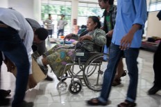 Supporters assist a protestor to move using a wheelchair while her feet remain cemented in a wooden crate. The Jakarta Post/Seto Wardhana