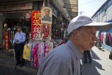 An elderly Chinese man walks past a security guard holding a prong for restraining attackers near a portrait of Mao Zedong and Cultural Revolution anti-soviet banners at a curio market in Beijing, China, Monday, May 16, 2016.  AP Photo/Ng Han Guan