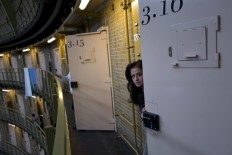 In this Saturday, May 7, 2016 photo, Afghan refugee Shazia Lutfi, 19, peeks through the door of her room at the former prison of De Koepel in Haarlem, Netherlands. The government has let Belgium and Norway put prisoners in its empty cells and now, amid the huge flow of migrants into Europe, several Dutch prisons have been temporarily pressed into service as asylum seeker centers. AP Photo/Muhammed Muheisen